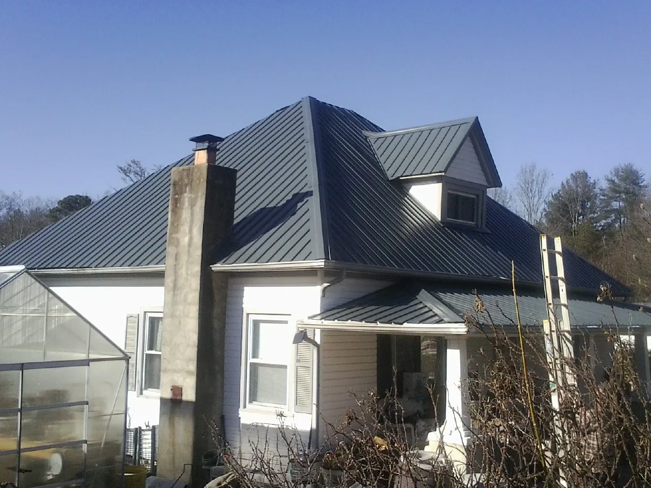 Dark blue standing seam metal roof on a white farmhouse with dormer — Slate & Tile Roof Repair by Roofing Brothers in West Middlesex