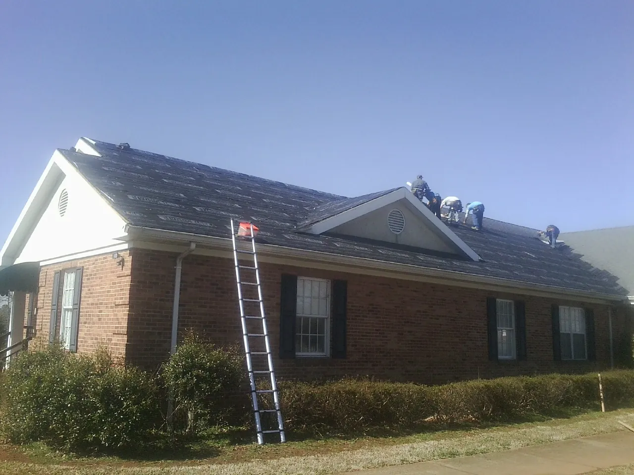 Crew tearing shingles off a brick ranch roof with a ladder set — Metal Roof Repair work by our crew in West Middlesex