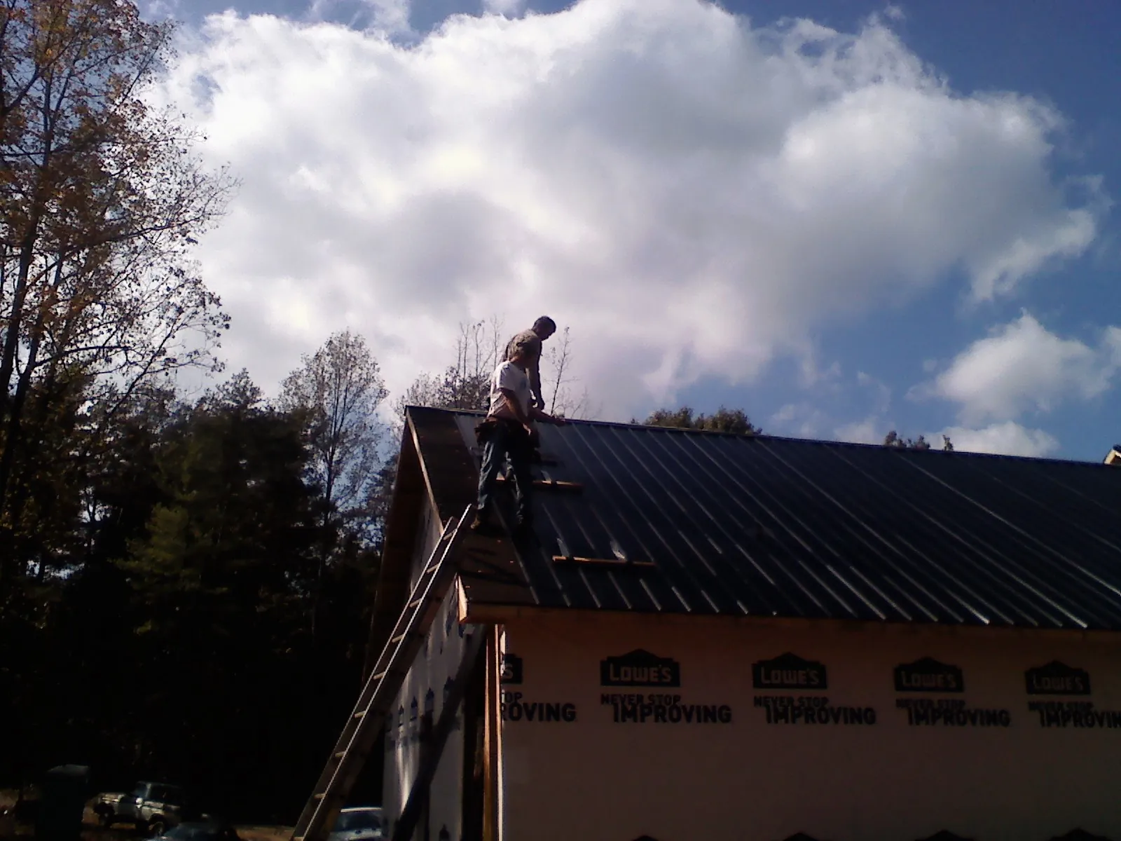 Roofer fastening dark metal panels high against a cloudy sky, from a Roof Inspection job in West Middlesex