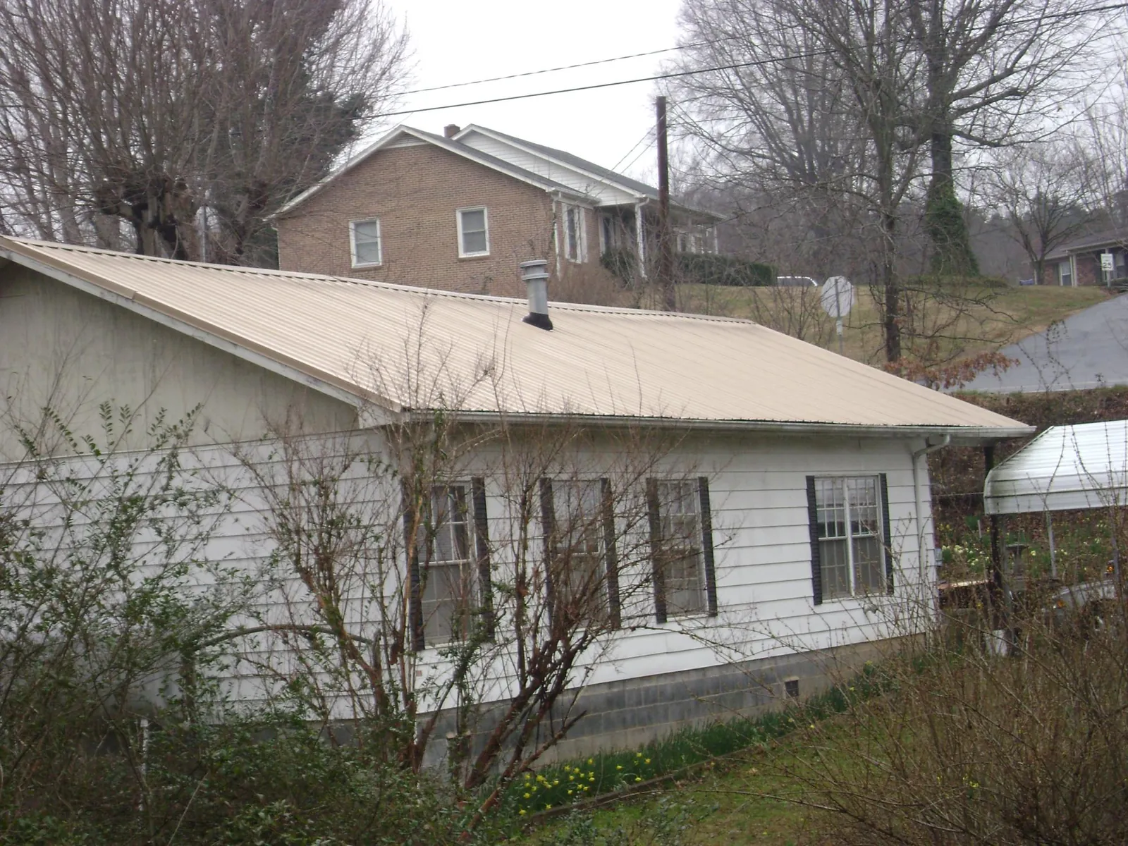 Tan metal roof on a white sided house set into a hillside — Commercial Roofing by Roofing Brothers in West Middlesex